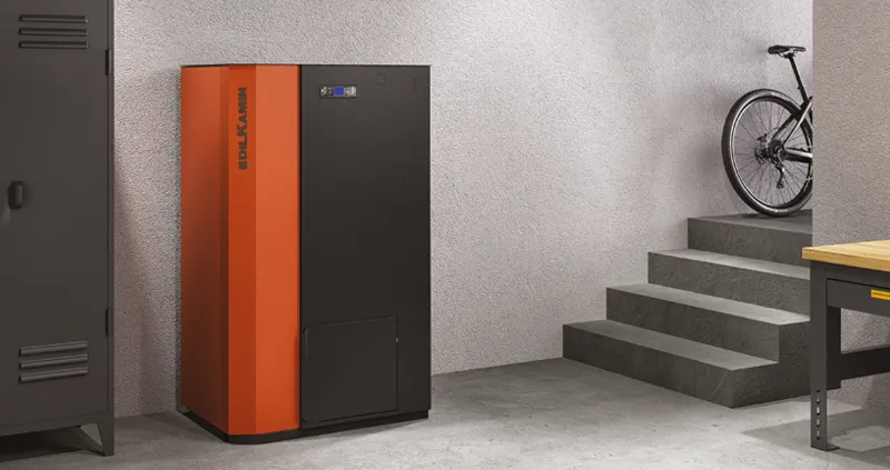 Caldaia Edilkamin Prisma H 22, color arancio e nero, in un seminterrato grigio, vicino ad un tavolo, un armadio e una bicicletta