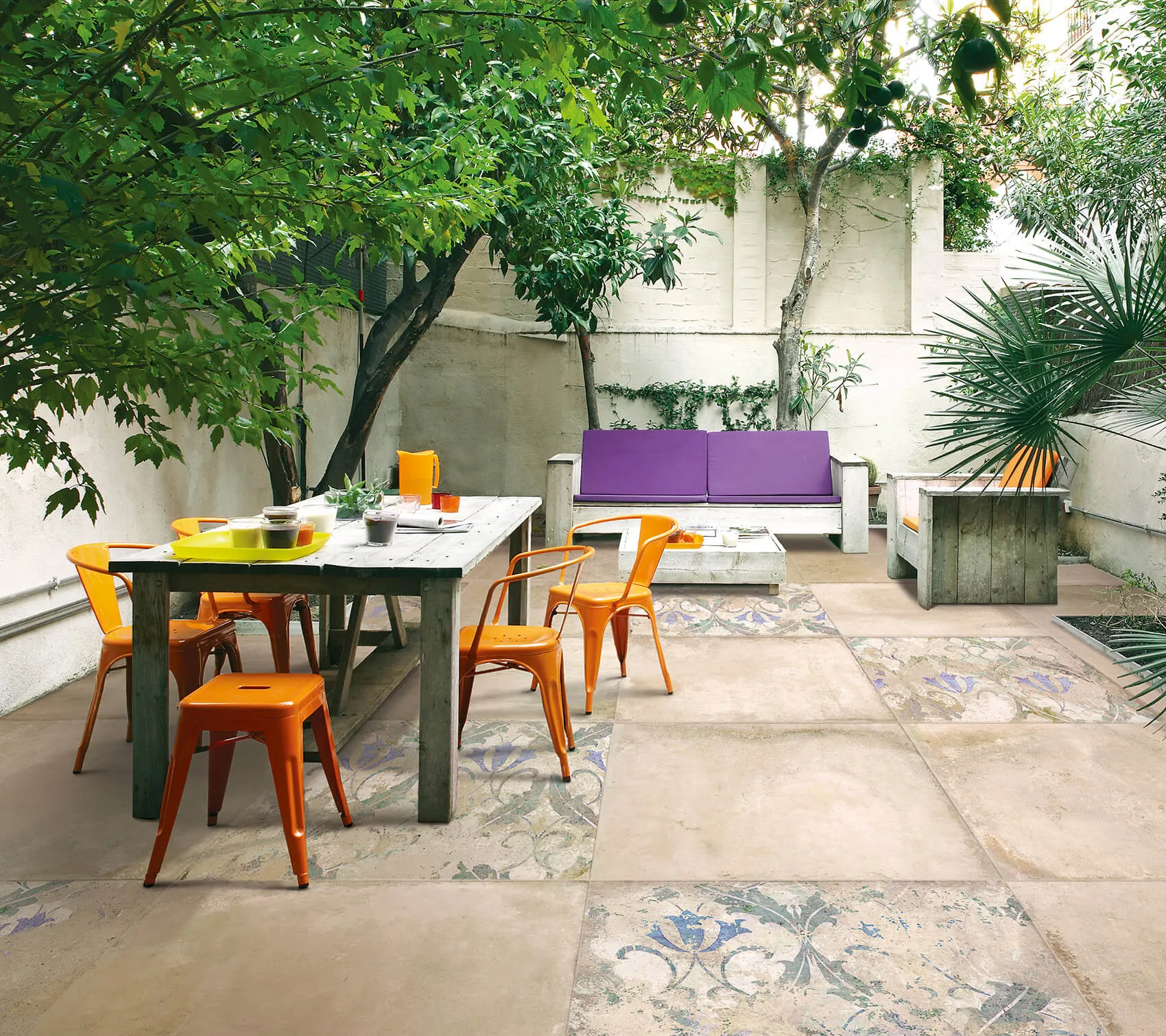 Esterno di una casa con un albero e piante verdi, pavimento in cotto tagina, un divano, tavolino e sedie colorati in viola e arancione